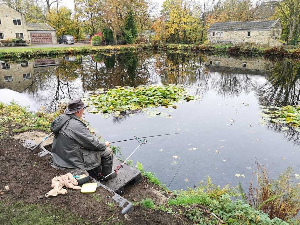 Man fishing, relaxing by a waterlilly filled pond pond.